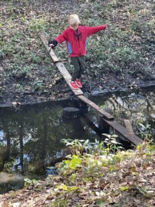 child crossing wooden planks over shallow creek