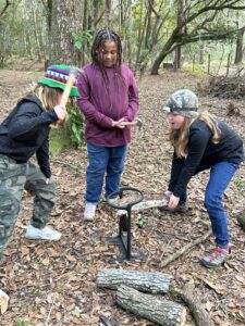 3 tween/teen girls using a log splitter in the forest