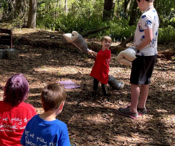 photo of 2 children jousting with a notable age difference and 2 children watching from the side