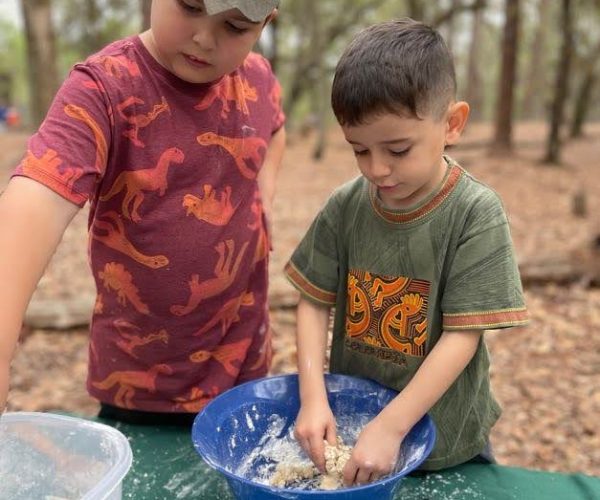 photo of 2 children of different sizes and ages playing in the mud kitchen