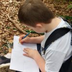 boy writing in a journal outside